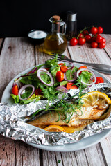 Mackerel baked in foil with vegetables on a plate. on a wooden background