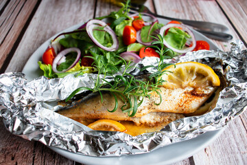 Fototapeta na wymiar Mackerel baked in foil with vegetables on a plate. on a wooden background