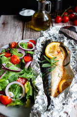 Obraz na płótnie Canvas Mackerel baked in foil with vegetables on a plate. on a wooden background
