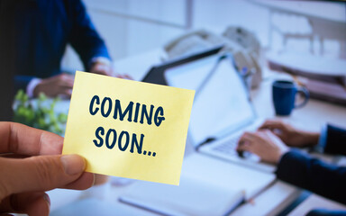 Male hand holding sticky note written Coming Soon.
