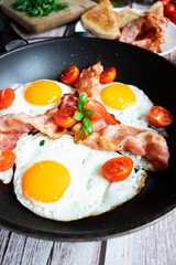 Fried eggs with bacon and fresh tomatoes. On a wooden background