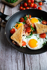Fried eggs with bacon and fresh tomatoes. On a wooden background