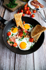 Fried eggs with bacon and fresh tomatoes. On a wooden background