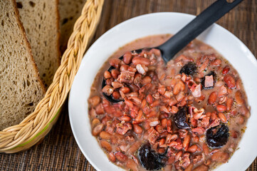 Legume soup from bean and plum in white plate, bread.