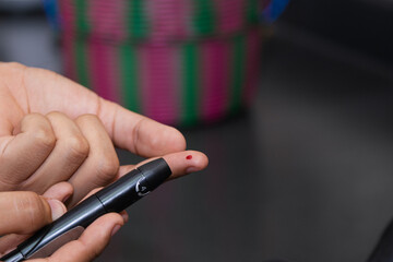 Young Latino man doing blood sugar test in the kitchen. Blood glucose test. Drawing blood for medical test. Using glucose meter in the kitchen.
