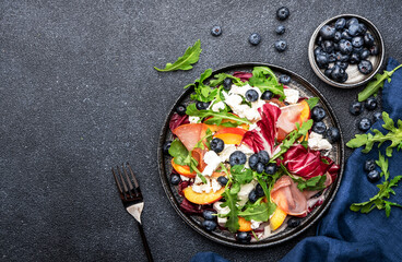 Delicious salad  with arugula, radicchio, peaches, prosciutto, feta cheese and blueberries. Black table background, top view