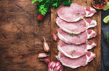 Raw pork chops on rustic wooden cutting board prepared for cooking with garlic, thyme, spices and...