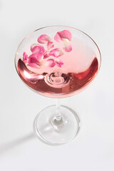 Rose wine with rose petals in a transparent glass. Rose petals. Rose wine in glass. Vertical photo on a white background. Isolated object.