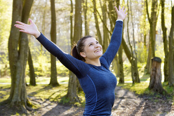 Cheerful athletic woman doing sports outdoor in a forest is happy about training progress and...