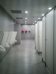 Large public pisshole with no one inside.  At the back attached to the bright red wall are two fans for drying hands.