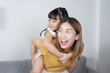 Happy Asian mother carry her daughter on her back in livingroom.