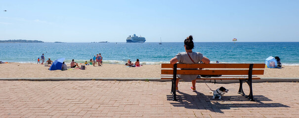 Cote d'Azur in Frankreich Sandstrand mit Frau und Hund auf Bank, Kreuzfahrtschiff im Hintergrund...