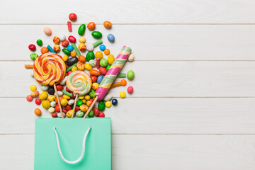 shopping paper gift bag in corner full of assorted traditional candies falling out on colored background with copy space. Happy Holidays sale concept