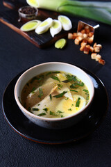 Fresh fish soup in a bowl on a black background, top view. White bread crackers. White fish soup. Transparent broth. A healthy dish. Lean menu.Vertical photo.Space for copying.Selective focus.