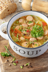 Fresh hot soup with meat sausage slices, beans, carrot, pasta and green herbs in bowl on wooden board.