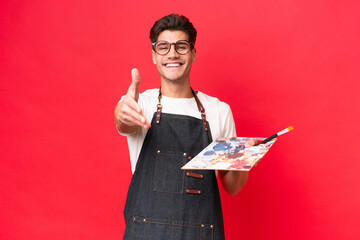 Young artist caucasian man holding a palette isolated on red background shaking hands for closing a...