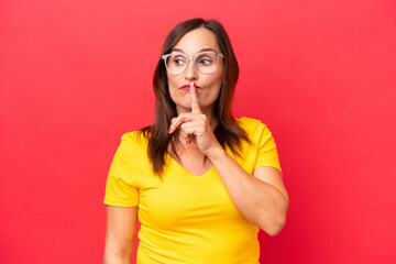 Middle-aged caucasian woman isolated on red background showing a sign of silence gesture putting finger in mouth