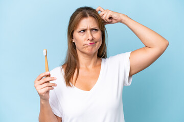 Middle-aged caucasian woman brushing teeth isolated on blue background having doubts and with...