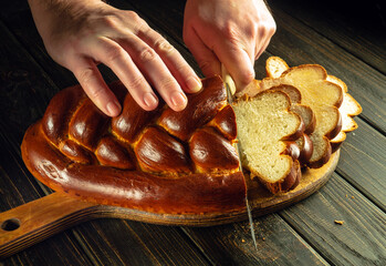 Chef hands cut with a knife fresh bread or kalach on a kitchen cutting board for lunch. Healthy food and traditional bakery concept