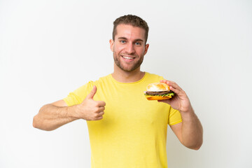 Young caucasian man holding a burger isolated on white background with thumbs up because something good has happened