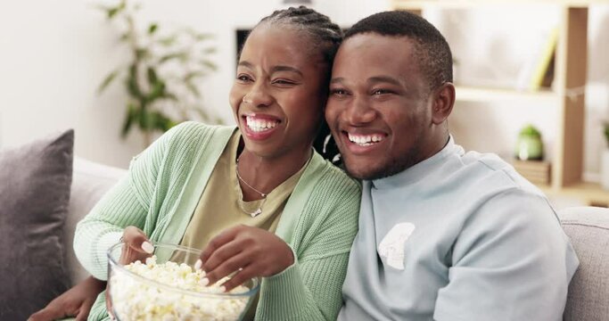 Popcorn, kiss and couple watching tv on a sofa, happy and bonding in their home. Love, snack and black woman with man on a couch for date, television or movie on streaming or subscription service