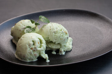 pistachio ice cream in a black waffle cone. Nutty green dessert with cinnamon sticks on a black background