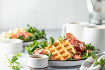 Cheesy belgian waffles served with ham, tomatoes and lettuce corn on white marble background . Savory waffles. Healthy breakfast. Text space