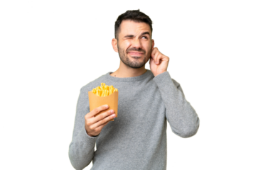 Young caucasian man holding fried chips over isolated chroma key background frustrated and covering ears