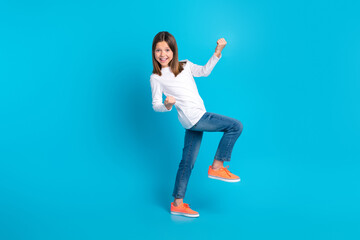Fototapeta na wymiar Full size photo of impressed cute girl wear white long sleeve denim trousers clenching fists pass exam isolated on blue color background