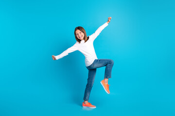 Fototapeta na wymiar Full length photo of friendly funny schoolgirl dressed white shirt jeans sneakers dancing have fun isolated on blue color background