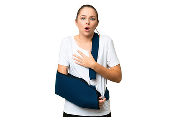 Young blonde woman with broken arm and wearing a sling over isolated chroma key background surprised and shocked while looking right