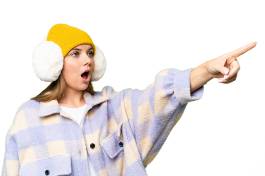 Young blonde woman wearing winter muffs over isolated chroma key background pointing away