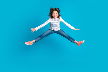 Fototapeta na wymiar Full size photo of pleasant funny cute girl wear white long sleeve denim trousers jumping flying isolated on blue color background