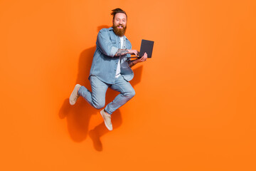 Full length photo of handsome excited guy jumping use netbook empty space isolated on orange color background