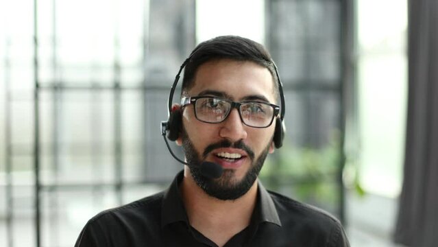 Cheerful friendly online technical operator agent with headphones and microphone talking with client in customer support office