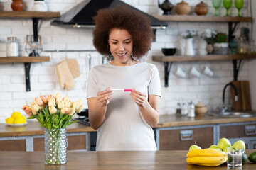 Smiling young happy african american woman at home looking at positive pregnancy test