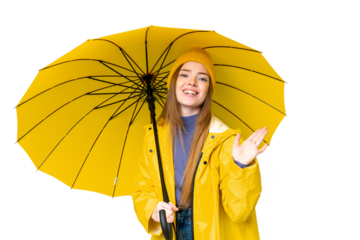 Young pretty woman with rainproof coat and umbrella over isolated chroma key background saluting with hand with happy expression
