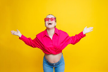 Happy pregnant woman with a smile on her face. Cheerful pretty pregnant woman in a pink shirt and pink glasses on a yellow background. Young bright pregnant woman.