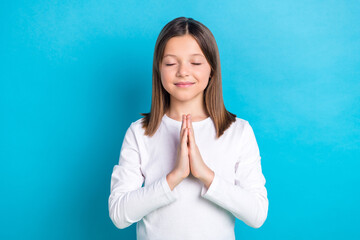 Photo of satisfied peaceful schoolgirl with straight hairdo dressed white shirt eyes closed praying isolated on blue color background
