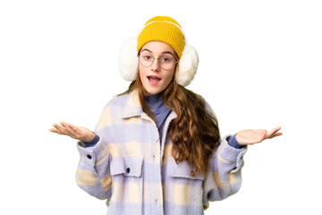 Teenager girl wearing winter muffs over isolated chroma key background with shocked facial expression
