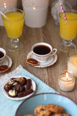 Plate of chocolate pralines, bowl of cookies, cups of tea, glasses of juice and lit candles on the table. Selective focus.