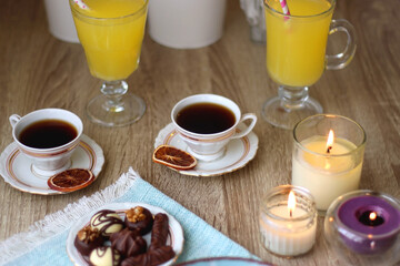 Plate of chocolate pralines, bowl of cookies, cups of tea, glasses of juice and lit candles on the table. Selective focus.