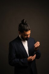 Hispanic elegant male with long hair buttoning his suit with black wall background