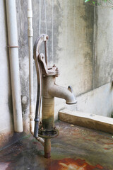 An old faucet for pumping water by hand near a building in India.