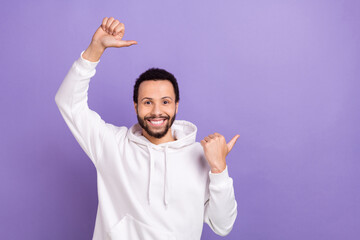 Fototapeta premium Photo of friendly man with curly hairstyle dressed white hoodie directing at offer empty space isolated on purple color background