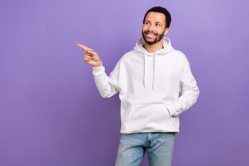 Portrait of cheerful guy with brunet beard wear white pullover directing look at discount empty space isolated on violet color background