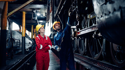 Team of engineer railway wearing safety uniform and helmet under checking under train ,wheels and...