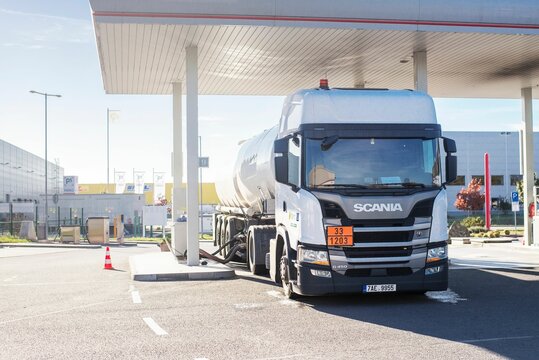 White fuel tanker truck at a petrol station connected by a hose to the underground tanks