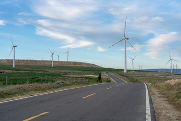 Fototapeta na wymiar Windmill farm among an empty highway under the clouds and blue sky