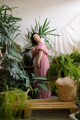 Charming landscape designer woman in pink off-the-shoulder dress enjoys beautiful plants in her greenhouse. Hobby. 